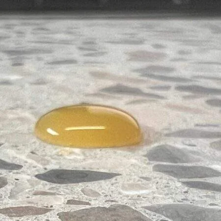Bestandsfoto: gelber Safttropfen auf einer Terrazzo-Probe – Abperlen belegt keinen Säureschutz