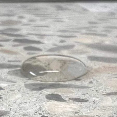 Bestandsfoto: klarer Wassertropfen auf einer Terrazzo-Probe – Beispiel für sichtbares Abperlverhalten